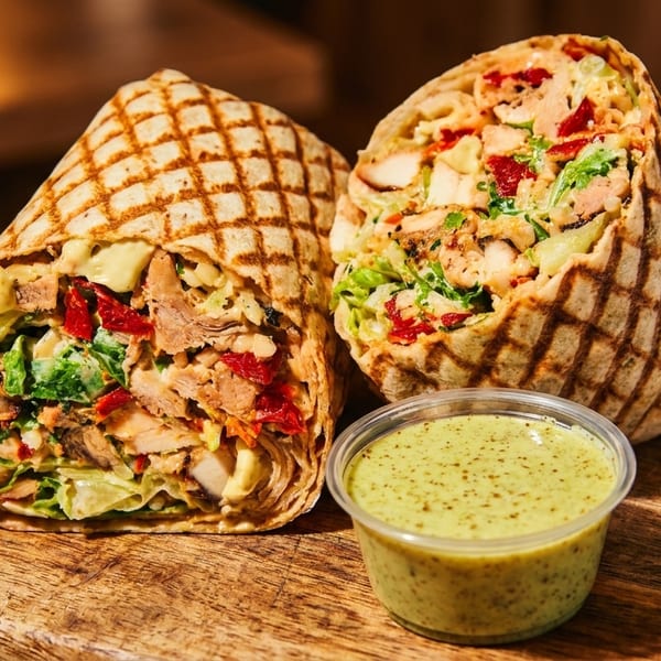 Two grilled chicken wraps with lettuce, sun-dried tomatoes, and avocado, served with green sauce.