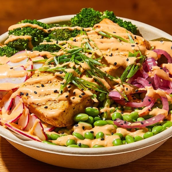 A colorful bowl with tofu, broccoli, radishes, edamame, pickled onions, and a creamy orange sauce.