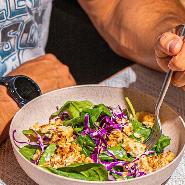 A person with a watch on their wrist eating a salad with spinach, red cabbage, and crumbled cheese.