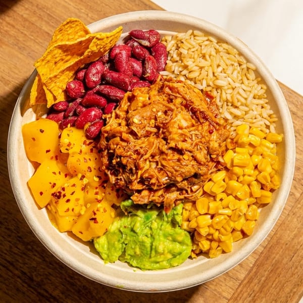 Vibrant bowl with pulled meat, brown rice, kidney beans, corn, guacamole, mango, and tortilla chips.