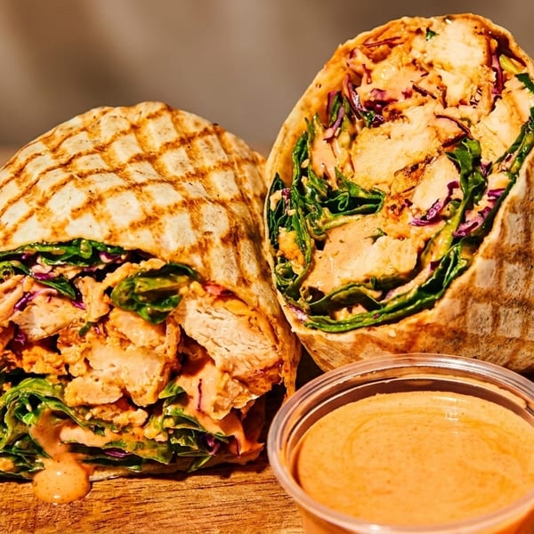 Two grilled chicken wraps with lettuce, red cabbage, and sauce, on a wooden surface.