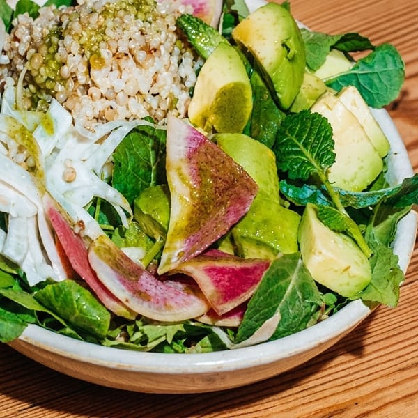 A vibrant salad bowl with greens, avocado, watermelon radish, and grains, next to a Big Wave soda.